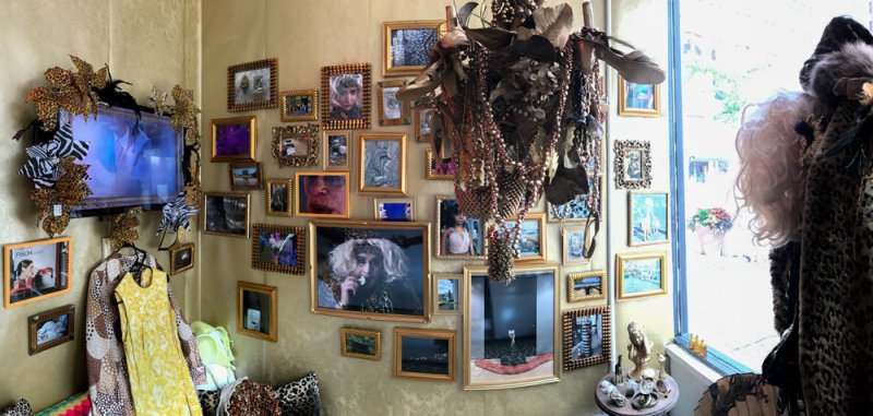A wall covered with various framed artworks, a television, and hanging objects, creating a maximalist collage.