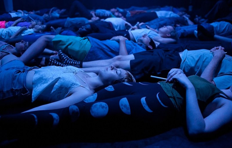 People lie on the floor in a dark room, illuminated by blue light.