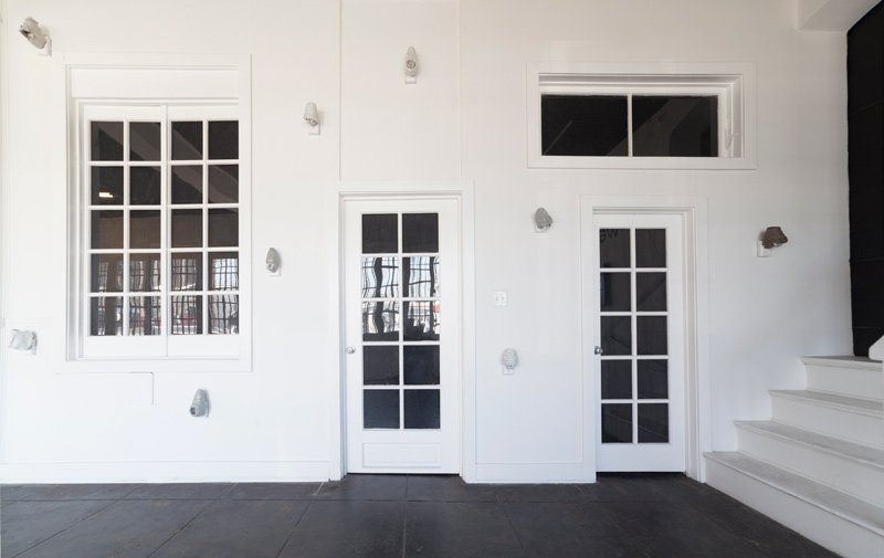 White room with dark floor, two doors, and two windows with multiple panes, and white steps on the right.