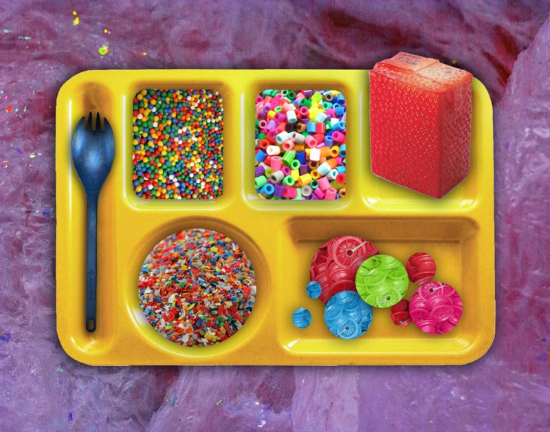 Yellow cafeteria tray with compartments of colorful sprinkles, beads, candy, and a red cube, on a purple glitter background.