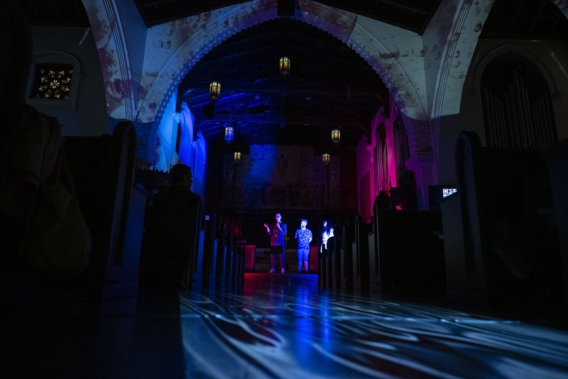 Scott N Andrew's "Vox Humana" (2024) shows a church interior bathed in blue and pink light, with figures on stage and projected patterns.