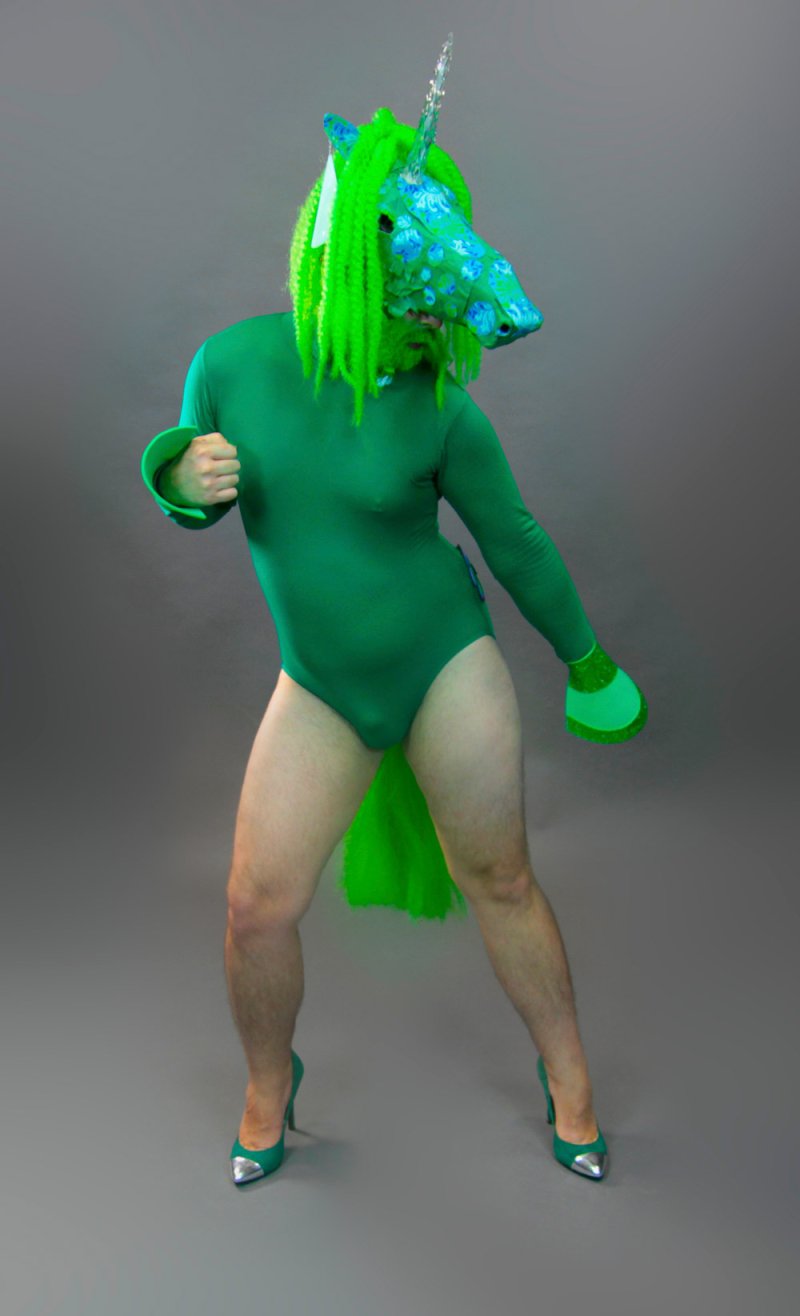 A person in a green bodysuit and matching heels poses against a gray background, wearing a blue floral unicorn mask with a bright green mane and tail.