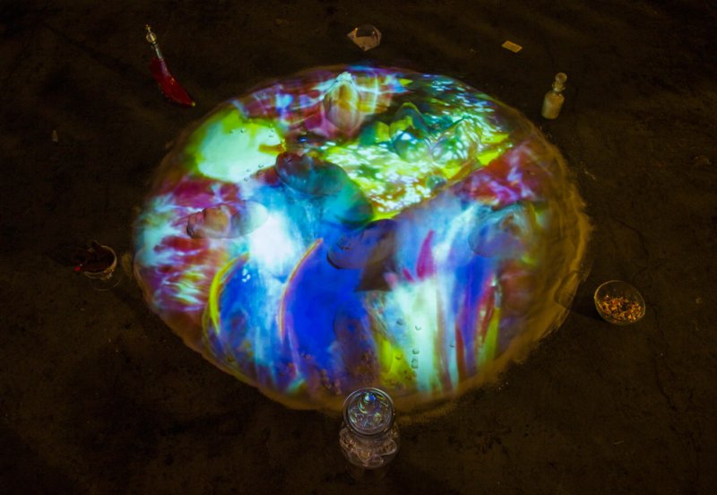 Overhead view of a circular, colorful projection on a dark floor, surrounded by small objects.