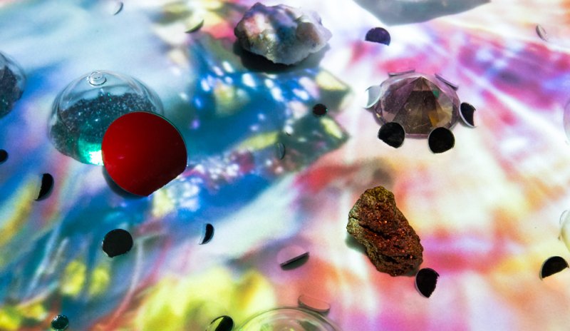 Installation with various objects on a surface illuminated by colorful, shifting light patterns.